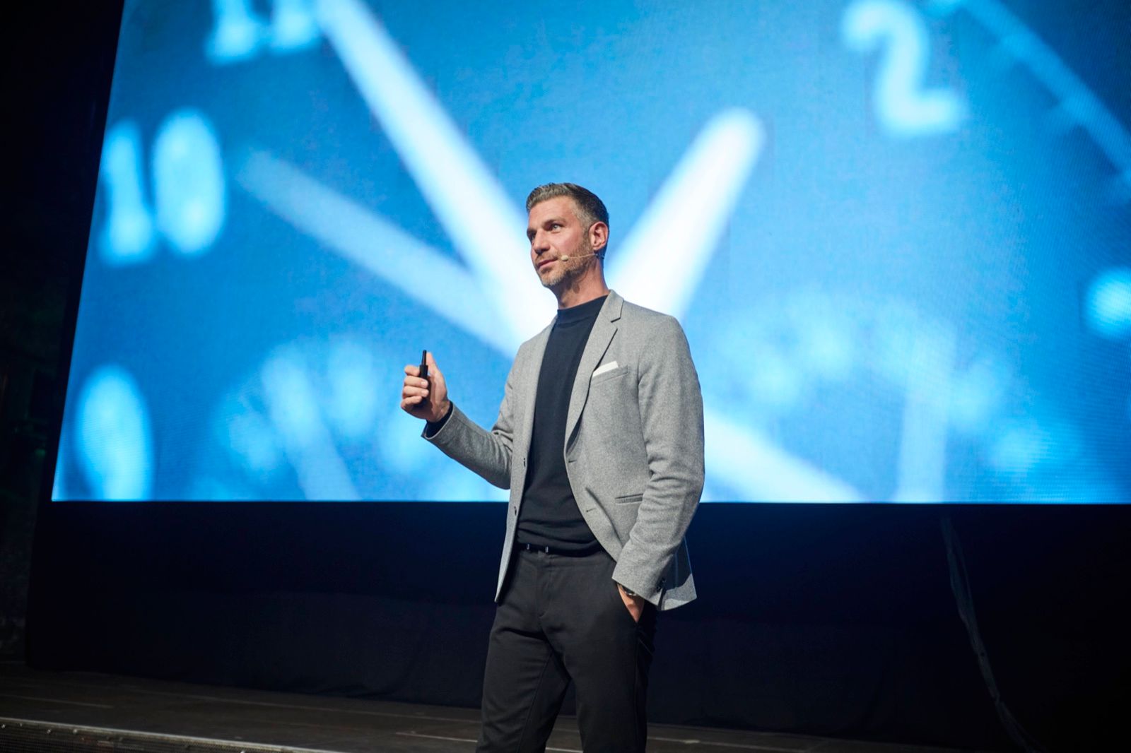 Florian Tenbusch auf der Bühne der Baufi Connect 2026, hinter ihm ein Zifferblatt auf der Leinwand